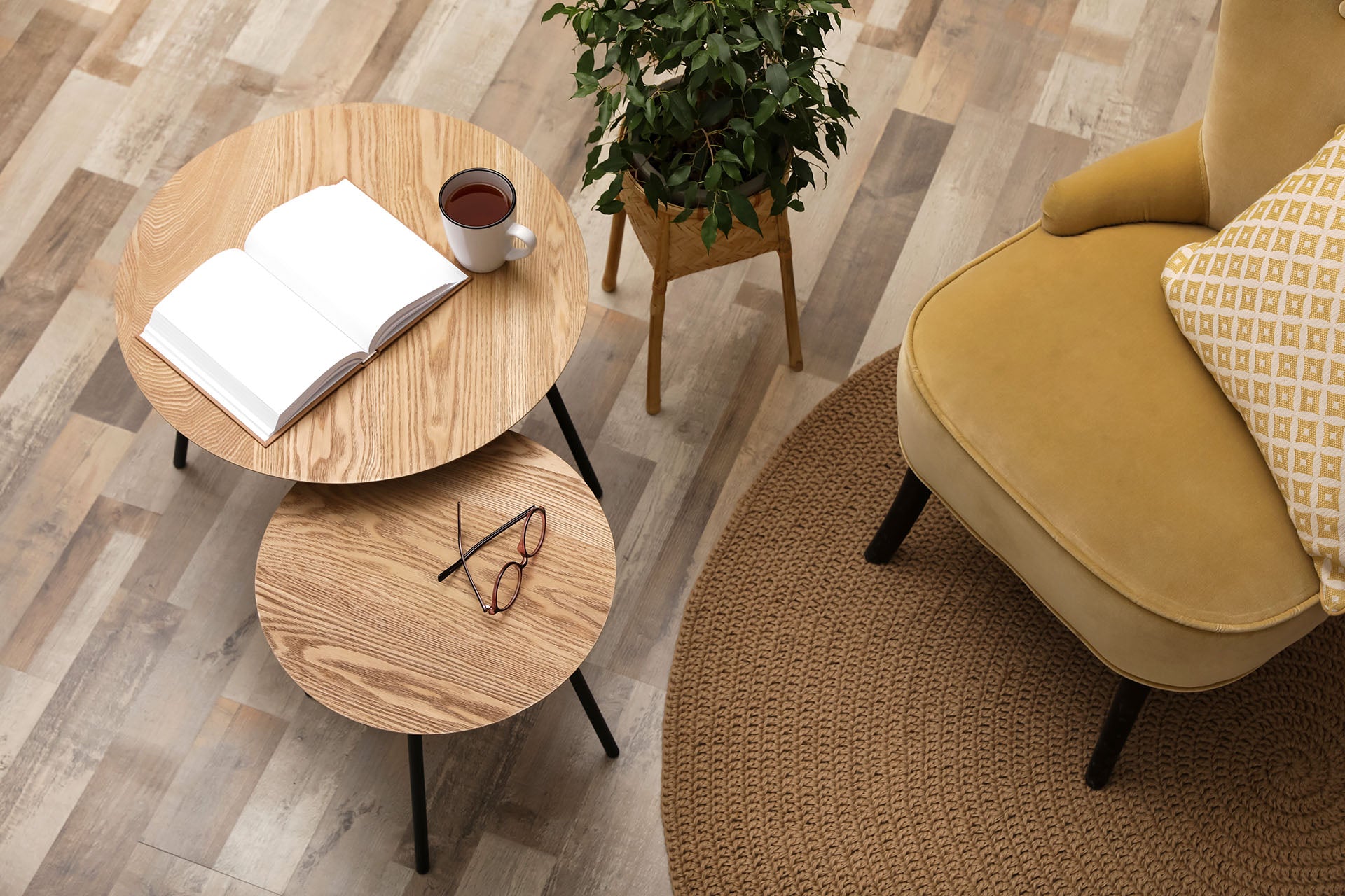 Wooden nest of tables showing two sizes, next to armchair and plant pot